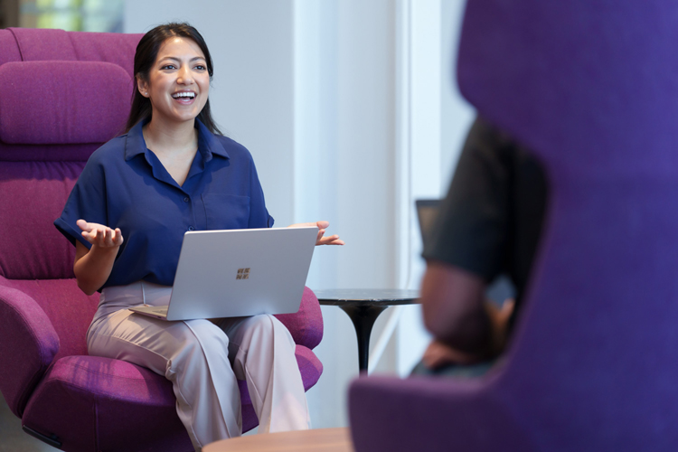 Smiling Insight employee sitting in lobby with laptop computer