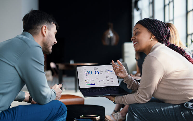 Two Insight colleagues collaborating on AI transformation data and project metrics displayed on a dashboard monitor.