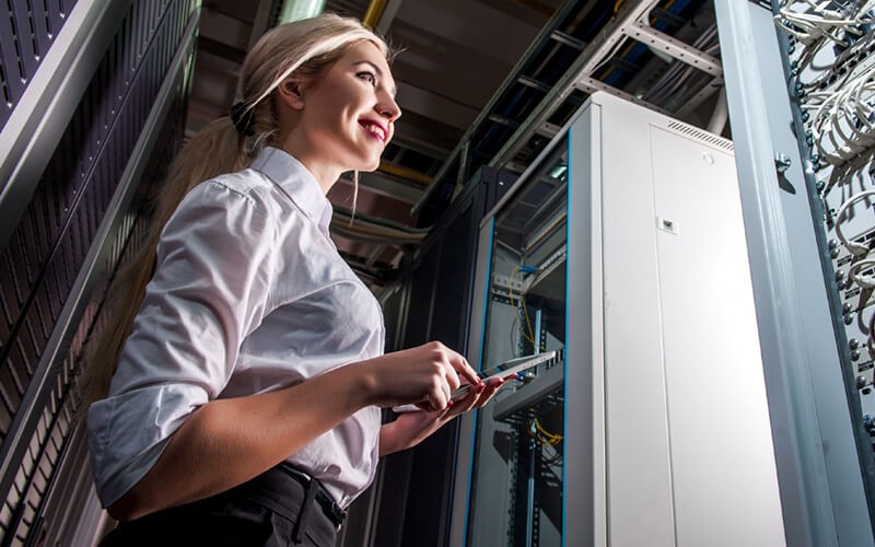 Smiling IT administrator on tablet in server rack room 