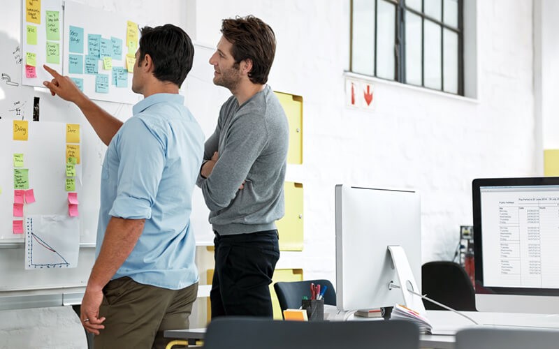 Two designers collaborating in office with sticky notes on whiteboard