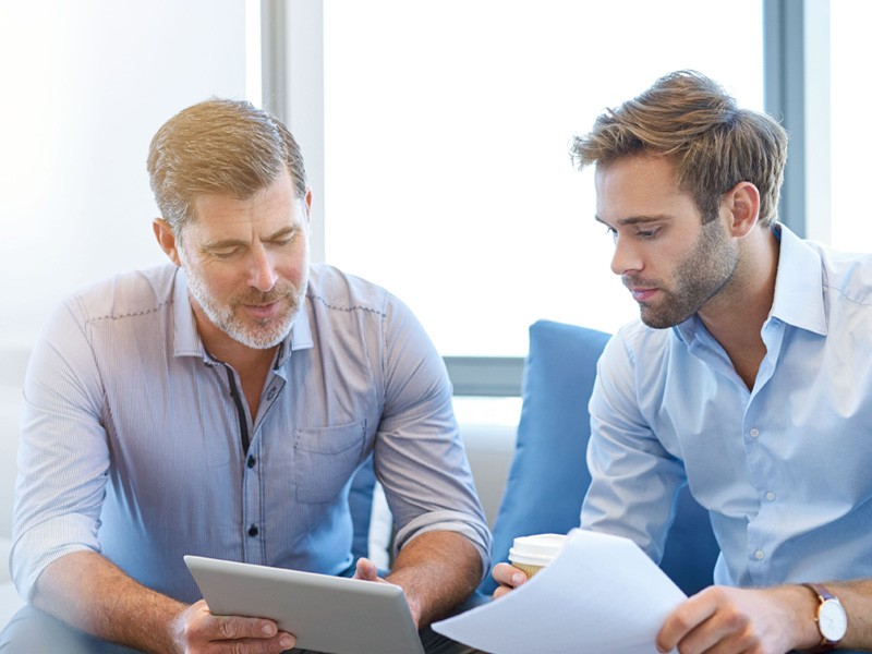 Business manager talking with direct report on couch in office holding technology financing agreements